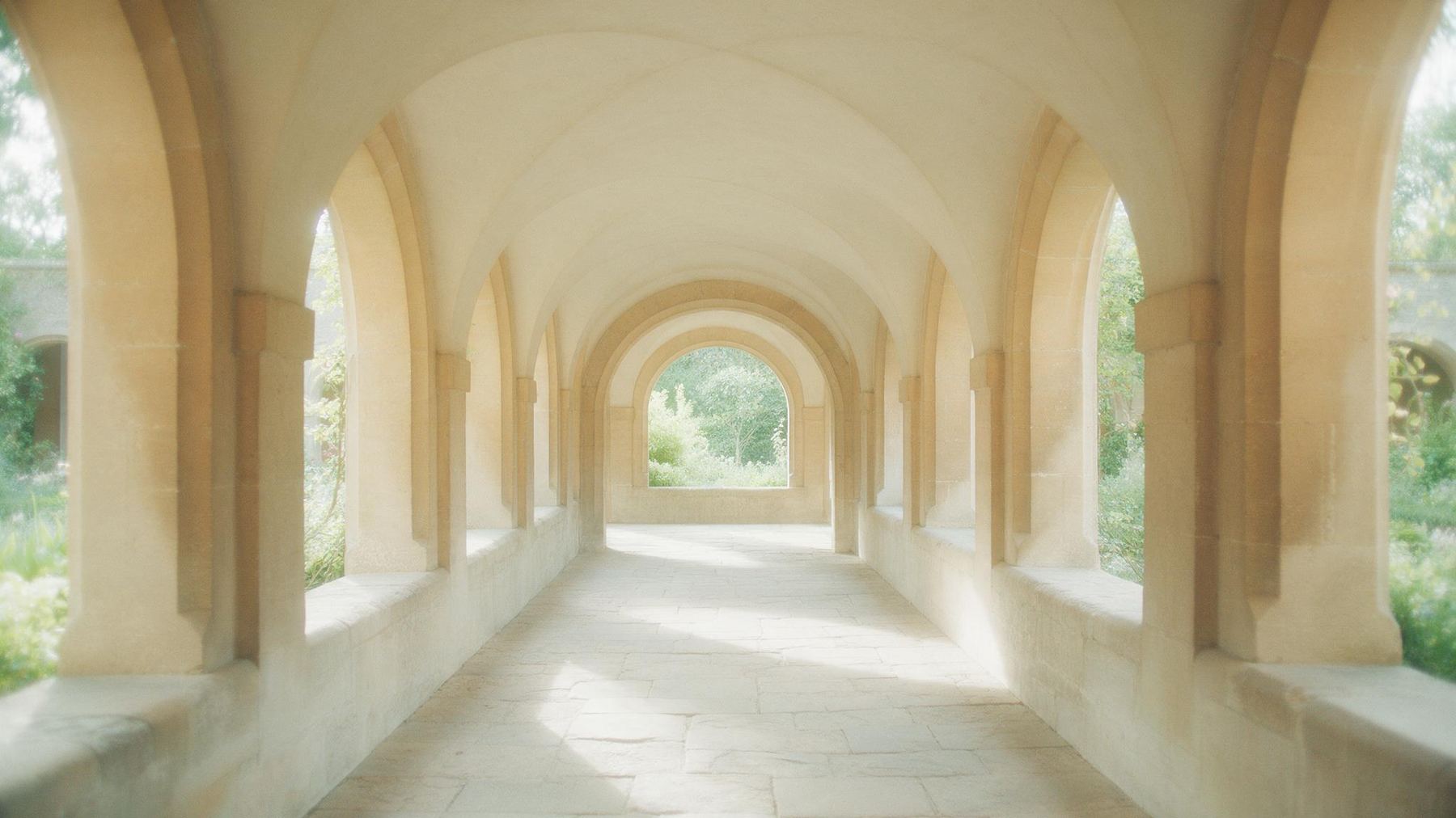 A stone cloister walkway in morning sunshine, garden light through the arches